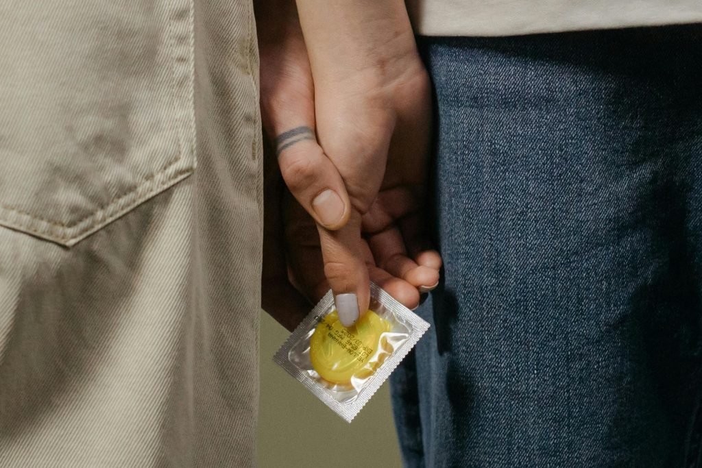 Close-up image of a couple holding hands with a condom, symbolizing safe sex.